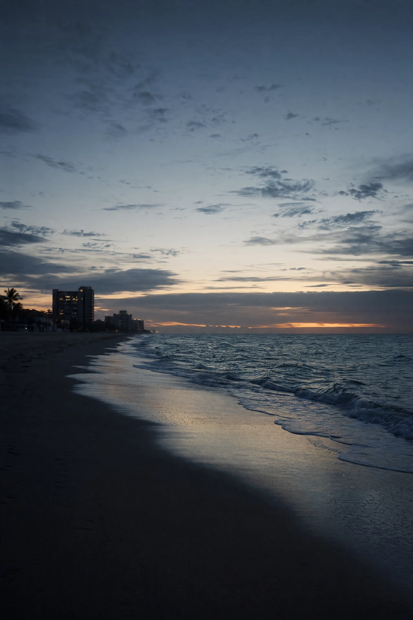 Empty Fort Lauderdale Beach shoreline before sunrise — the first orange light at the horizon, the city still dark